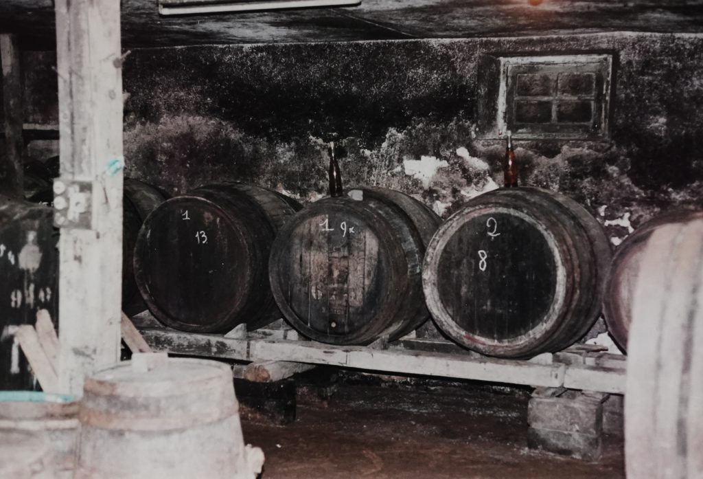 Cave voûtée avec de grands tonneaux en bois numérotés et bouteilles posées dessus