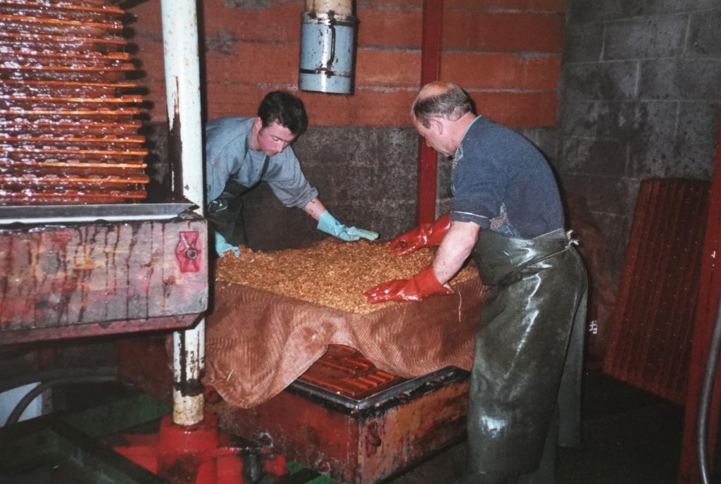 Deux hommes étalant la pulpe de pommes sur le pressoir traditionnel