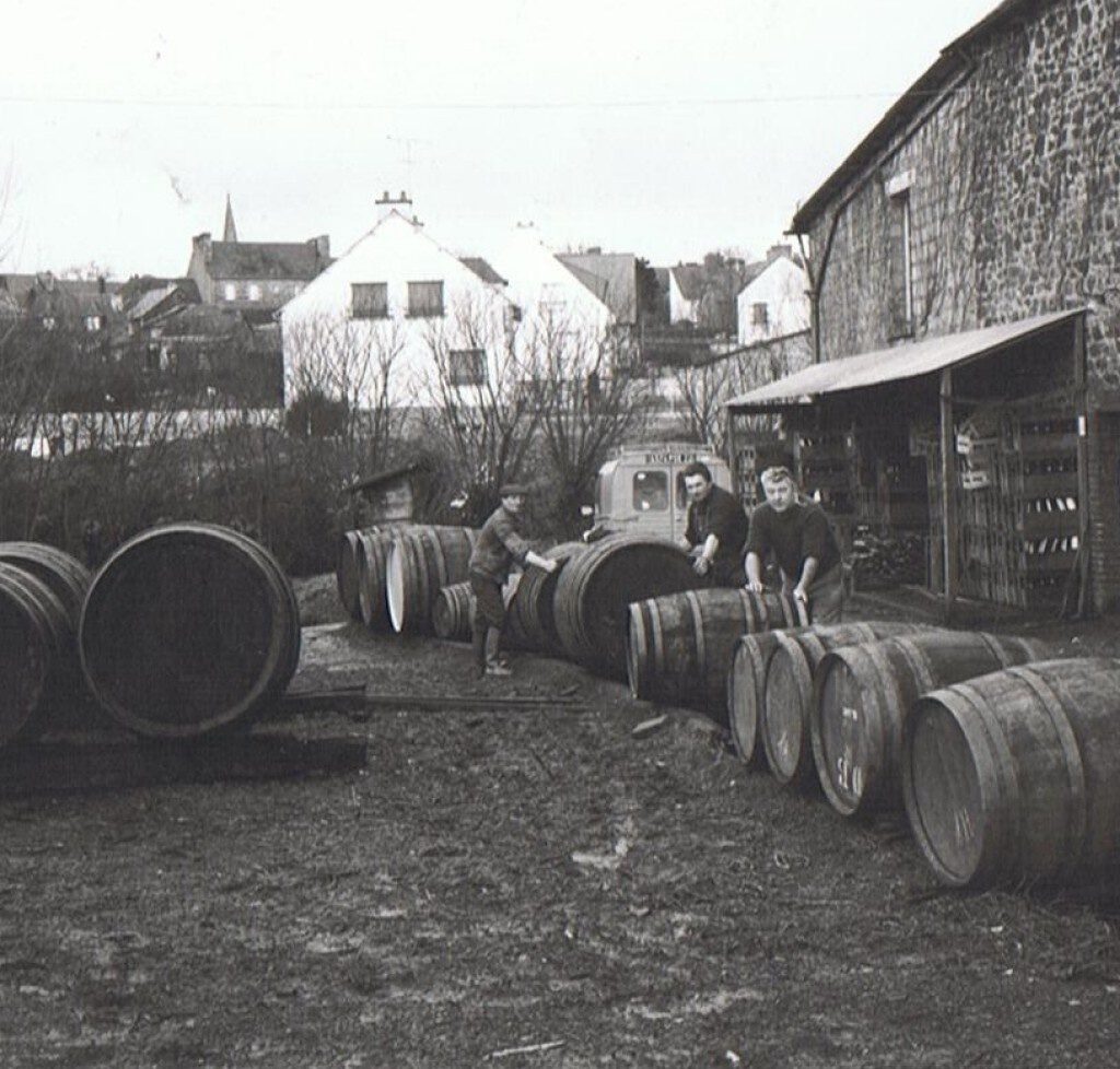 Trois hommes déplaçant des tonneaux en bois dans la cour de la cidrerie, photo historique noir et blanc