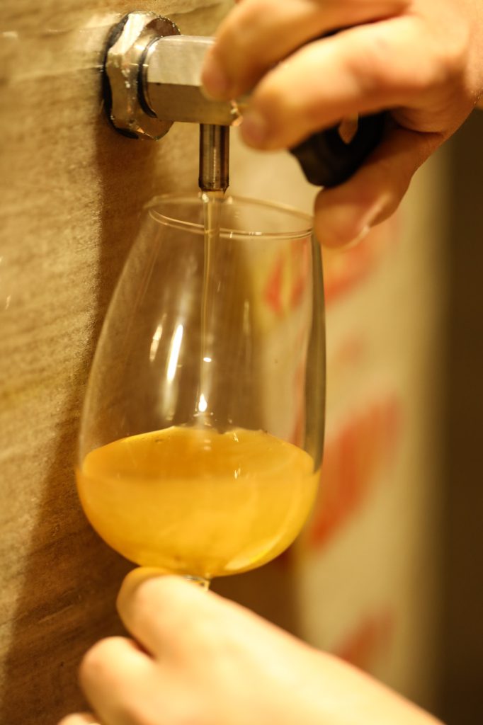 Cidre ambré versé au fausset d'une cuve en bois dans un verre tulipe