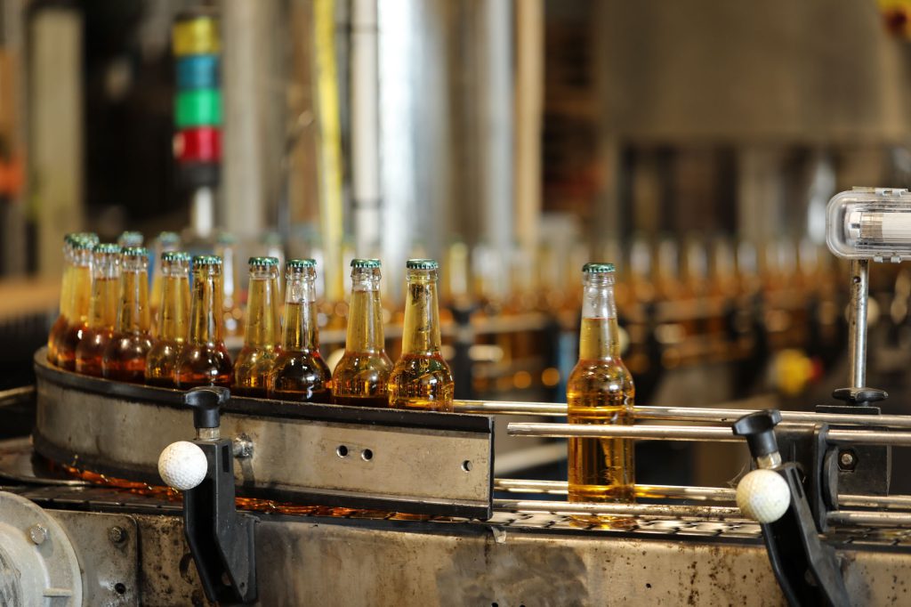 Bouteilles de cidre ambré capsulées vert sur convoyeur avec cuves en arrière-plan